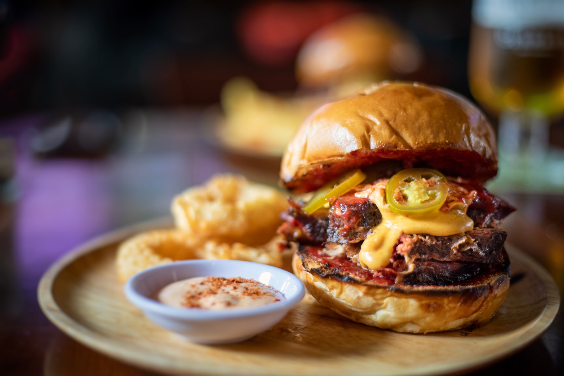 A meat sandwich with cheese, sliced green chilli, onion rings and sauce.